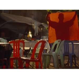  Man Holds Up a Tablecloth and Sets Tables at an Outdoor Restaurant 